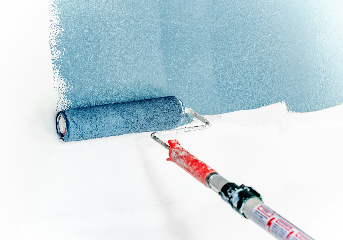 Paint roller applying a fresh coat of blue paint to a wall